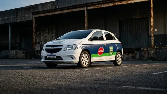 Veículo hatchback envelopado em hero frontal — plotagem de frota com luz dourada em galpão industrial